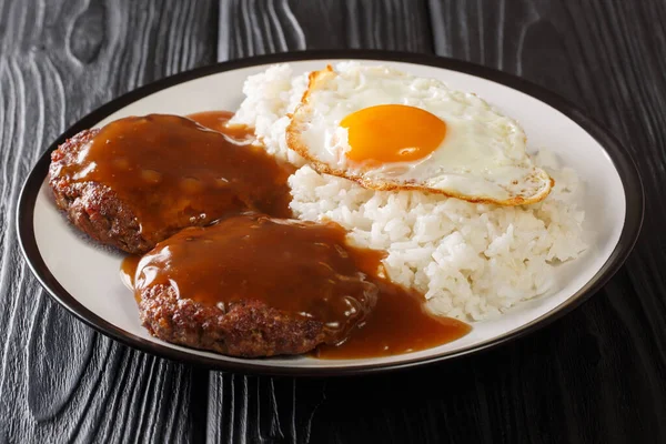 loco moco is a Hawaiian cuisine made with white rice with a hamburger patty, sunny side up egg, and brown beef gravy close-up on a plate on the table. Horizonta