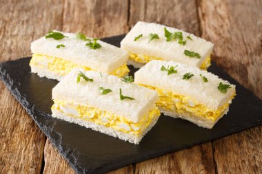 Beyaz ekmek dilimlerinin arasına sıkıştırılmış yumurta salatası, masadaki tahtaya yakın plan Japon yumurtalı sandviç Tamago Sando. Yatay