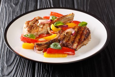 Masadaki tabakta ızgara domuz pirzolası, dolma biber, soğan ve fesleğen yakın plan. yatay