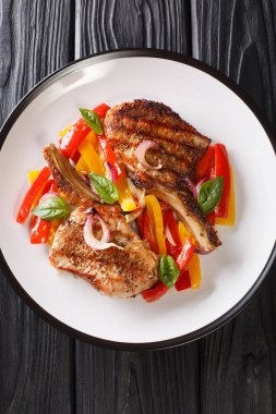 Kemiğin üzerinde ızgara domuz pirzolası, masada sarı ve kırmızı dolma biber ve soğan ile servis ediliyor. Yukarıdan dikey üst görünüm