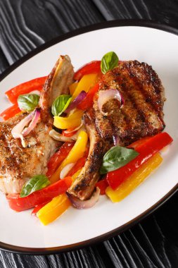 Kemiğin üzerinde ızgara domuz pirzolası, masada sarı ve kırmızı dolma biber ve soğan ile servis ediliyor. dikey