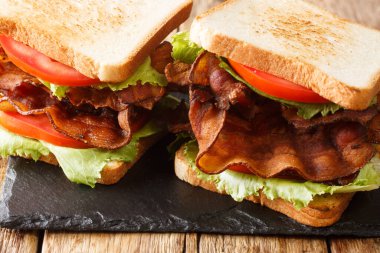 Geleneksel Amerikan sandviçi, domuz pastırmalı, salatalı ve domatesli masaya yakın plan. yatay