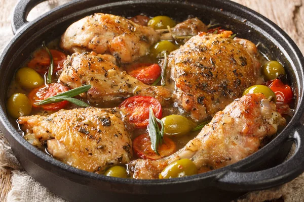 Delicious chopped chicken baked with green olives, tomatoes and onions, herbs close-up in a frying pan on the table. horizonta