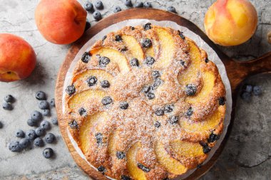 Masadaki tahta tahtaya yakın plan şeker serpiştirilmiş taze şeftali ve yaban mersini serpiştirilmiş yaz süngeri pastası. Yukarıdan yatay üst görünüm