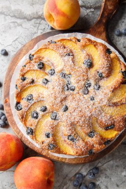 Böğürtlenli şeftalili kek yumuşak, nemli ve masanın üzerindeki tahta tahtaya yakın plan meyve aromasıyla dolup taşıyor. Yukarıdan dikey üst görünüm