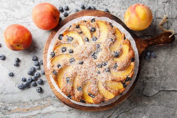 tatlı ve basit şeftali ve yabanmersinli kek. Masanın üzerindeki tahtanın üzerinde basit bir vanilyalı sünger kapağı var. Yukarıdan yatay üst görünüm