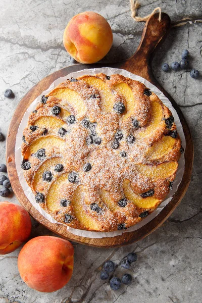 Masadaki tahtada taze yaz meyvesi yakın planlı yaban mersini şeftalili kremalı pasta. Yukarıdan dikey üst görünüm