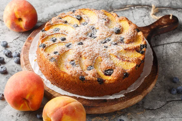 Masadaki tahta tahtaya yakın plan şeker serpiştirilmiş taze şeftali ve yaban mersini serpiştirilmiş yaz süngeri pastası. yatay