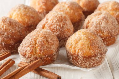 Taze pişmiş Fransız Puf kekleri erimiş tereyağında yuvarlandı ve ahşap masaya yakın plan tarçın şekeri ile kaplandı. Yatay