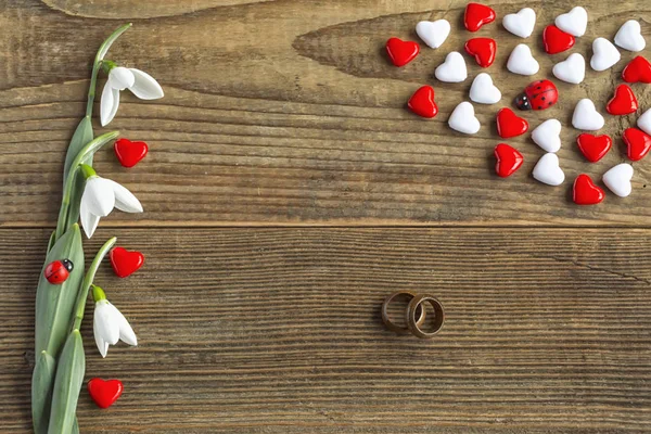 Valentines day romantic concept of red and white hearts with two wooden wedding rings symbolize endless love of two persons decorated with fresh snowdrops on wooden vintage background.