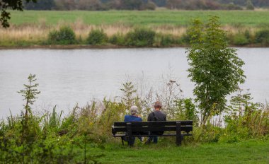 Nehir kenarındaki bankta oturan olgun bir çift.