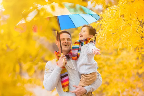 A little boy and his father are under a colorful umbrella. Family in warm clothes and colorful scarves. the kid catches the rain drops with his palm