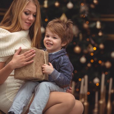 Çocuk elinde bir Noel hediyesiyle annesinin kucağında oturuyor. Tatil bekliyorum.