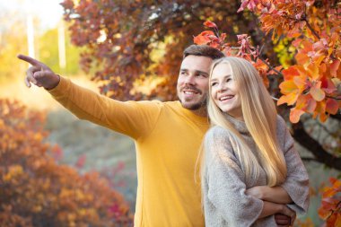 Sarı kazaklı, sakallı genç bir adam uzun saçlı bir sarışına sarılıyor. Tatilde olan evli bir çift. Balayı