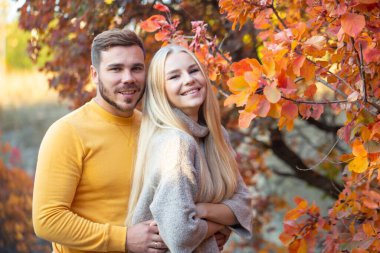 Sarı kazaklı, sakallı genç bir adam uzun saçlı bir sarışına sarılıyor. Tatilde olan evli bir çift. Balayı