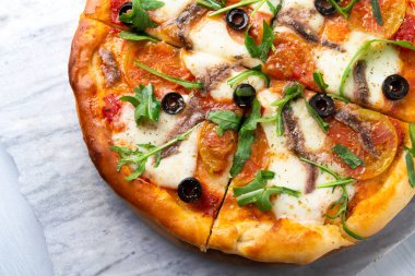 Mozzarella, domates sosu, zeytin, hamsi ve roka salatası ile lezzetli dilimlenmiş sıcak pizza 