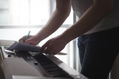 Besteci ve söz yazarı notlar veya şarkı sözleri piyano kağıda yazılı. Müzisyen dijital enstrüman ev stüdyosunda bir şarkı yazmak. Yeni bir fikir veya melodi hakkında heyecanlı. Gölgeli karanlık ortam yıldırım.