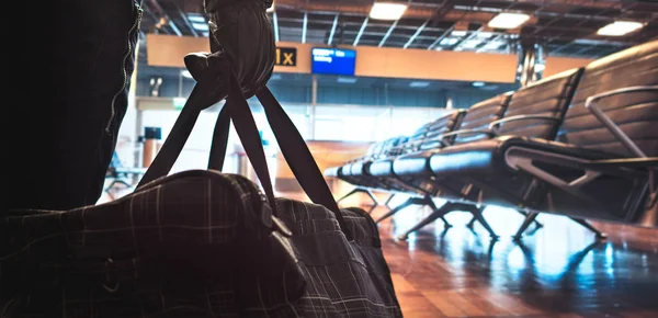 Terrorism in aiport. Dangerous terrorist planning a bomb attack in the waiting area and gate. Holding suspicious black bag with leather gloves. Anonymous criminal. Safety and security threat concept.