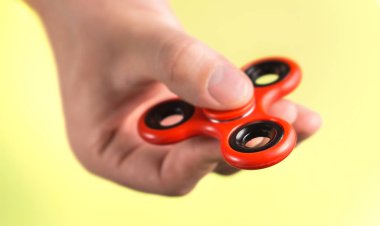 Kırmızı kıpır spinner uçuk sarı arka plana karşı parmakları arasında.