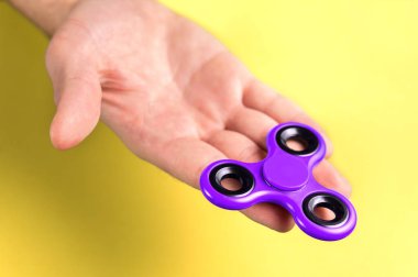 Mor ve menekşe spinner el, palmiye ve parmak sarı arka plana karşı kıpır.