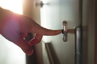 Parmak basarak kapı zili güneşli apartman koridorda. Erkek el bir blok daireler içinde kapı zili çalmayı kapat. Satıcı, fundraiser, Konuk veya ziyaretçi kapının arkasında.