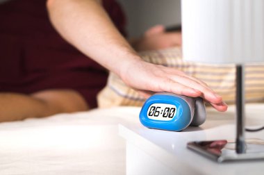 Adam yatağında uyanmak. Çalar saat komodinin üzerinde devre dışı bırakarak veya erteleme tuşuna basarak.