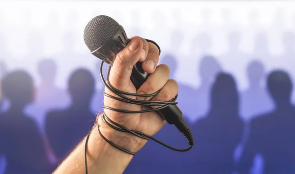 Stage fright in public speaking or bad karaoke singing live in front of crowd of people. Problem with speech or failed talent show performance. Microphone wire, cable and cord wrapped around hand.
