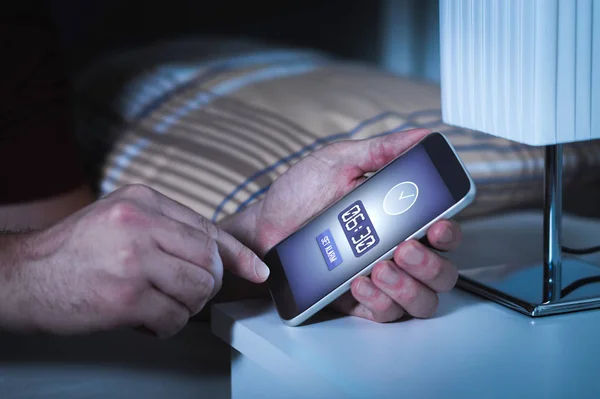 Man setting alarm to smartphone before going to sleep at night. Clock in mobile phone. Wake up early to work next morning.