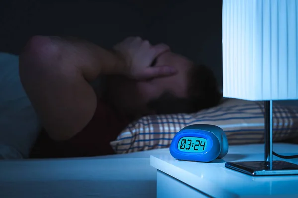 不眠症と不眠のコンセプト 人間は眠ることができません 疲れと疲れ 手で顔を覆っています ナイト テーブル 寝室のベッドのアラーム時計 — ストック写真