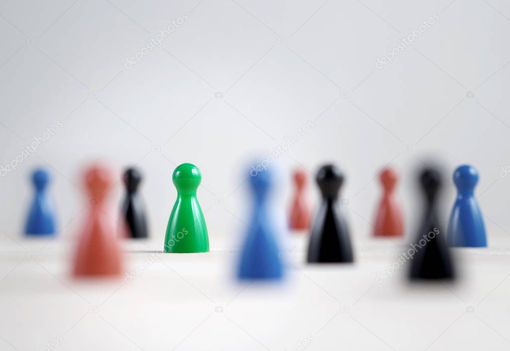 Many board game pawns on table, selective focus on the green one. Being brave, be yourself and originality concept. Diversity and tolerance.