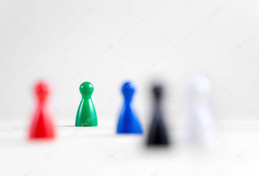 Many board game pawns on table, selective focus on the green one. Being brave, be yourself and originality concept. Diversity and tolerance.