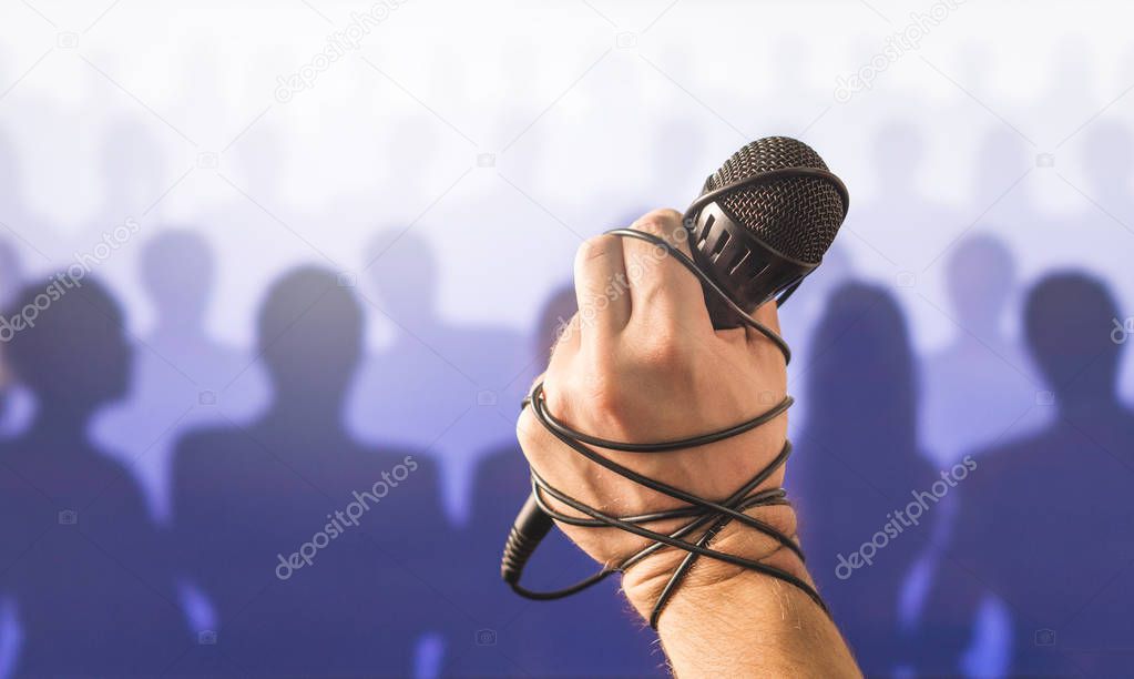 Stage fright in public speaking or bad karaoke singing live in front of crowd of people. Problem with speech or failed talent show performance. Microphone wire, cable and cord wrapped around hand.