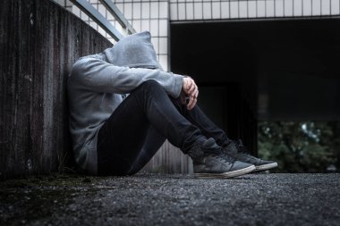 Depresyon, sosyal izolasyon, yalnızlık, ruh sağlığı ve ayrımcılık kavramı. Üzgün, yalnız, depresif ve mutsuz adam. Kukuletalı kişi karanlık sokakta oturuyor.