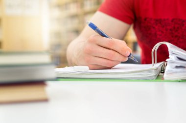 Genç atletik erkek ve eğitim ve genel veya okulda kütüphane Koleji ya da Üniversitesinde notlar yazma öğrenci. Yığın ve yığın kitap, kalem ve kağıt üzerinde tablo.