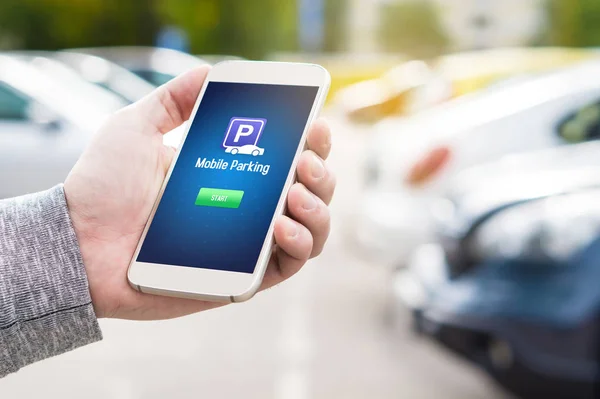 Mobile parking app on smartphone screen. Man holding smart phone with car park application in hand. Internet payment online with modern device. Row of vehicles in the background.