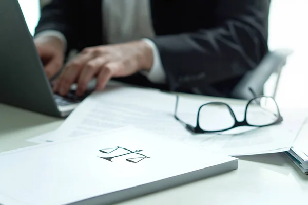 律师在办公室工作 律师用手提电脑写一份法律文件 桌子上戴着眼镜 一堆纸的规模和正义的象征 律师事务所与企业理念 — 图库照片