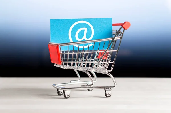 Online shopping, e commerce and internet store concept. Newsletter and email marketing. Miniature shopping cart with at sign.
