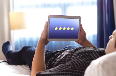 Bir daha gözden geçirme ve 5 star rating mobil uygulama ile. Müşteri memnuniyeti anketi ve geribildirim uygulaması tablet. Ev yatak odası ya da otel odasında modern akıllı aygıt kullanan adam.