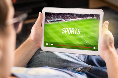 Man watching sports on tablet. Football and soccer game live stream and video player on screen. Pay per view (PPV) service. Replay or highlights broadcast. Lazy person relaxing. Couch potato. clipart