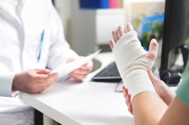Injured patient showing doctor broken wrist and arm with bandage in hospital office or emergency room. Sprain, stress fracture or repetitive strain injury in hand. Nurse helping customer. First aid. clipart