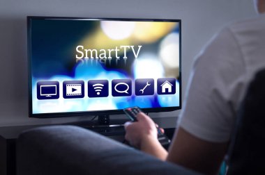 Akıllı tv izleyen adamım. Film ya da dizi menüsünden seçerek. Kişi holding uzaktan kumanda. Televizyon ekranında Kullanıcı arabirimi.