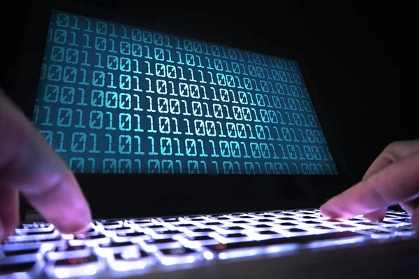 Hacker writing virus code with laptop in dark. Data crimimal in shadow. Cyber security, internet fraud and phishing concept. Close up of hands on keyboard and computer screen with binary numbers.