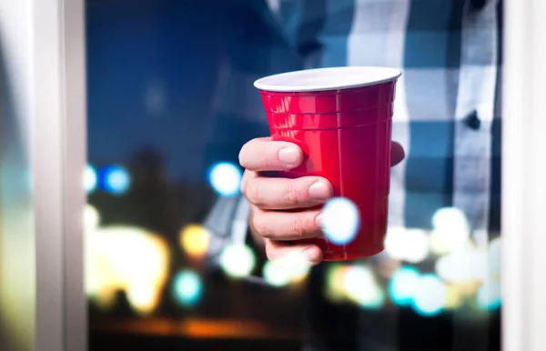 在豪华或大学聚会上举行红杯的男子 有乐趣或周末概念 酒吧或夜总会阳台窗口与城市灯反射 — 图库照片