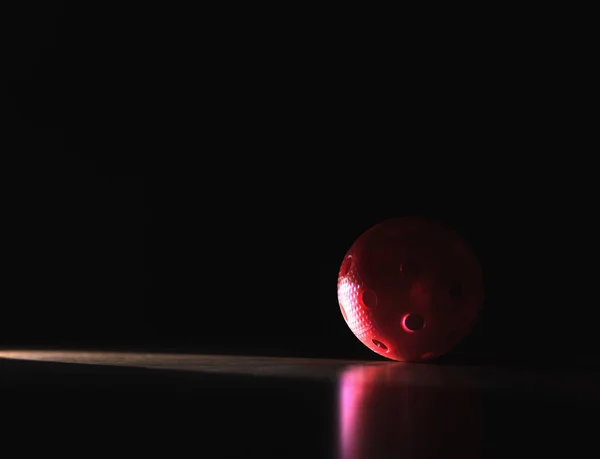 Black and dark floorball background with negative copy space. Red ball in spotlight in shadow.