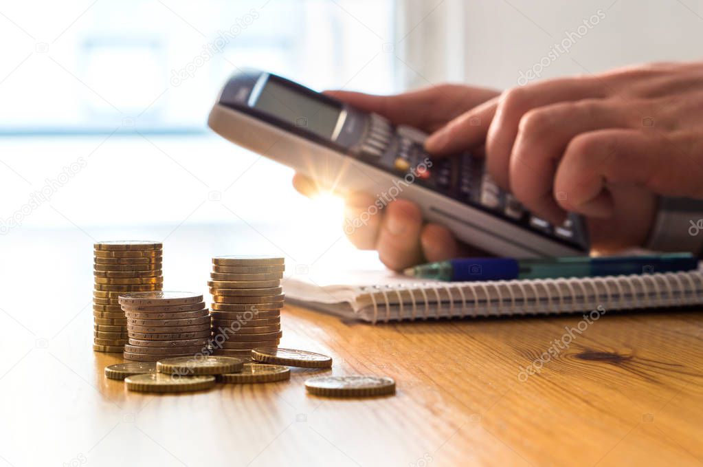 Man using calculator to count money savings and living costs. Inflation, taxes and rising expenses. Calculating daily family groceries price and budget. Stack of coins on table.