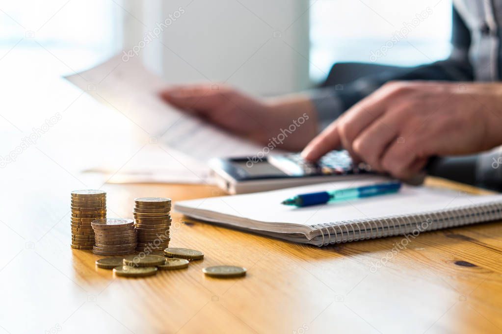 Man using calculator and reading financial document paper. Entrepreneur, bookkeeper or accountant working and counting tax, vat, loan, debt, savings or salary. Busy businessman paying bills at desk.