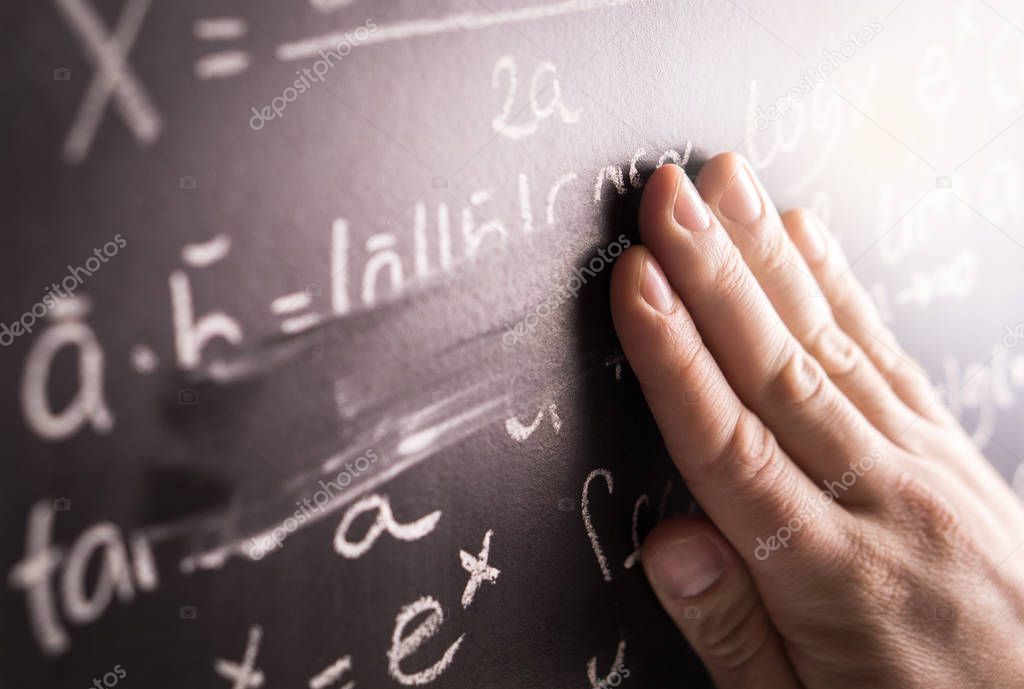 Making mistakes and wrong answer concept. Hand wiping math formula off blackboard in classroom at school. Student or teacher correcting incorrect calculation on chalkboard.