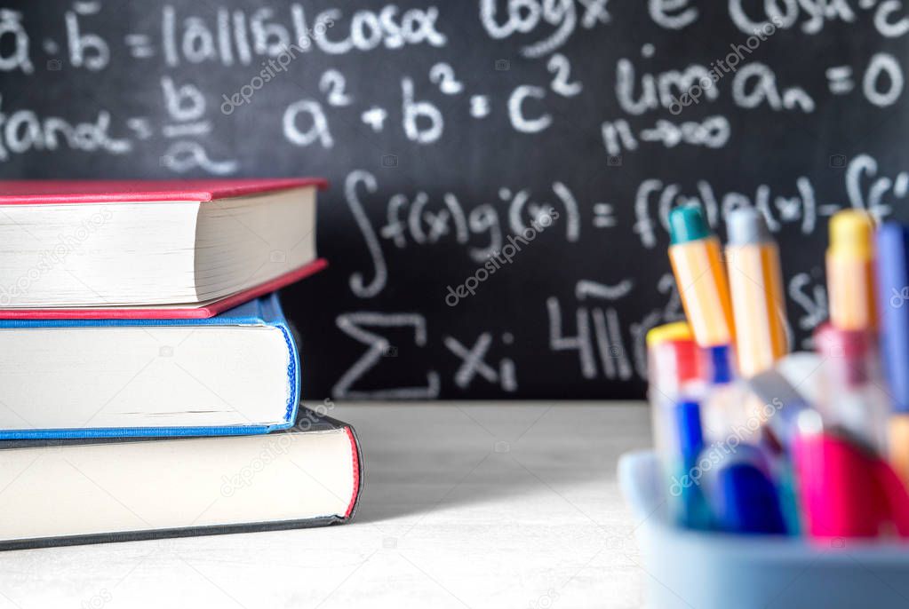 School supplies in classroom. Blackboard or chalkboard in class. Teaching, lesson, lecture and science concept. Math equation written in the background.