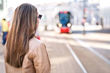 Arkadan görünüşü tramvay durdurmak için bekleyen kadın. Gelen city adlı seyir yolcu tren istasyonunda. Banliyö veya öğrenci ya da toplu taşıma kullanarak.