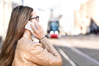 Tramvay için beklerken bir telefon sahip meşgul iş kadını. Şehir sokak smartphone ayakta olan kadın. Elektrikli tren içinde belgili tanımlık geçmiş.